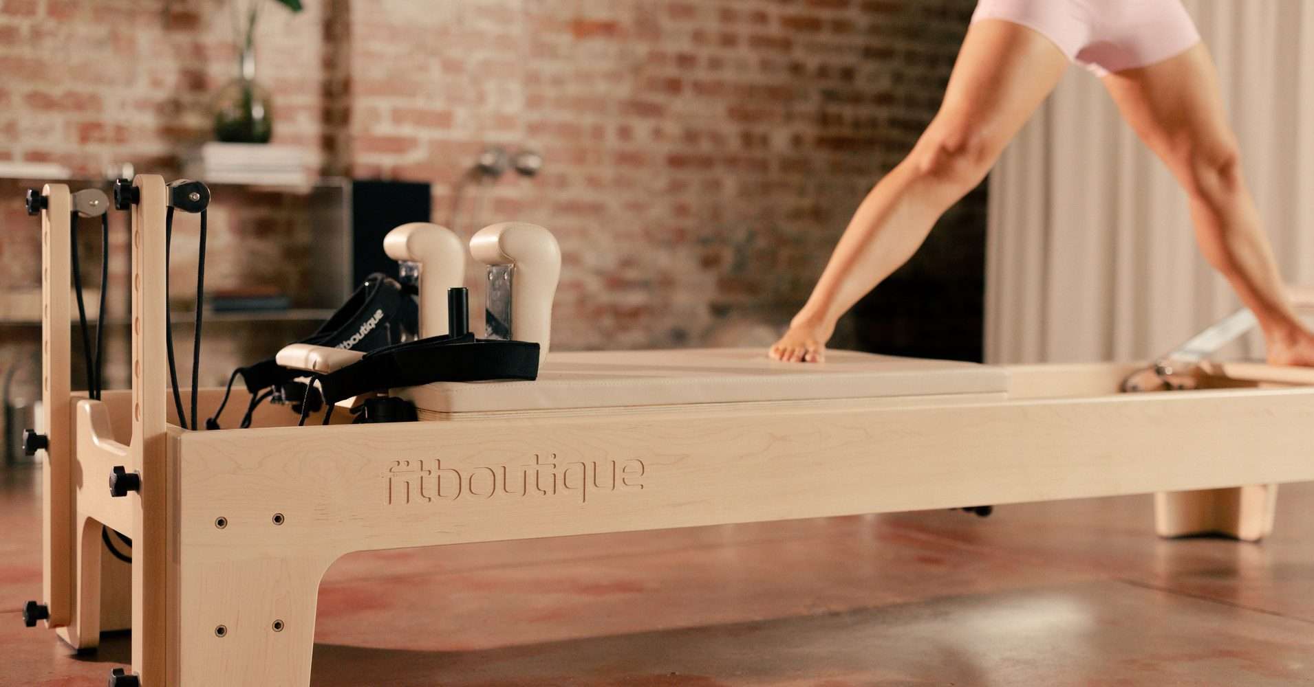 Standing side stretch on a FitBoutique black reformer in a studio