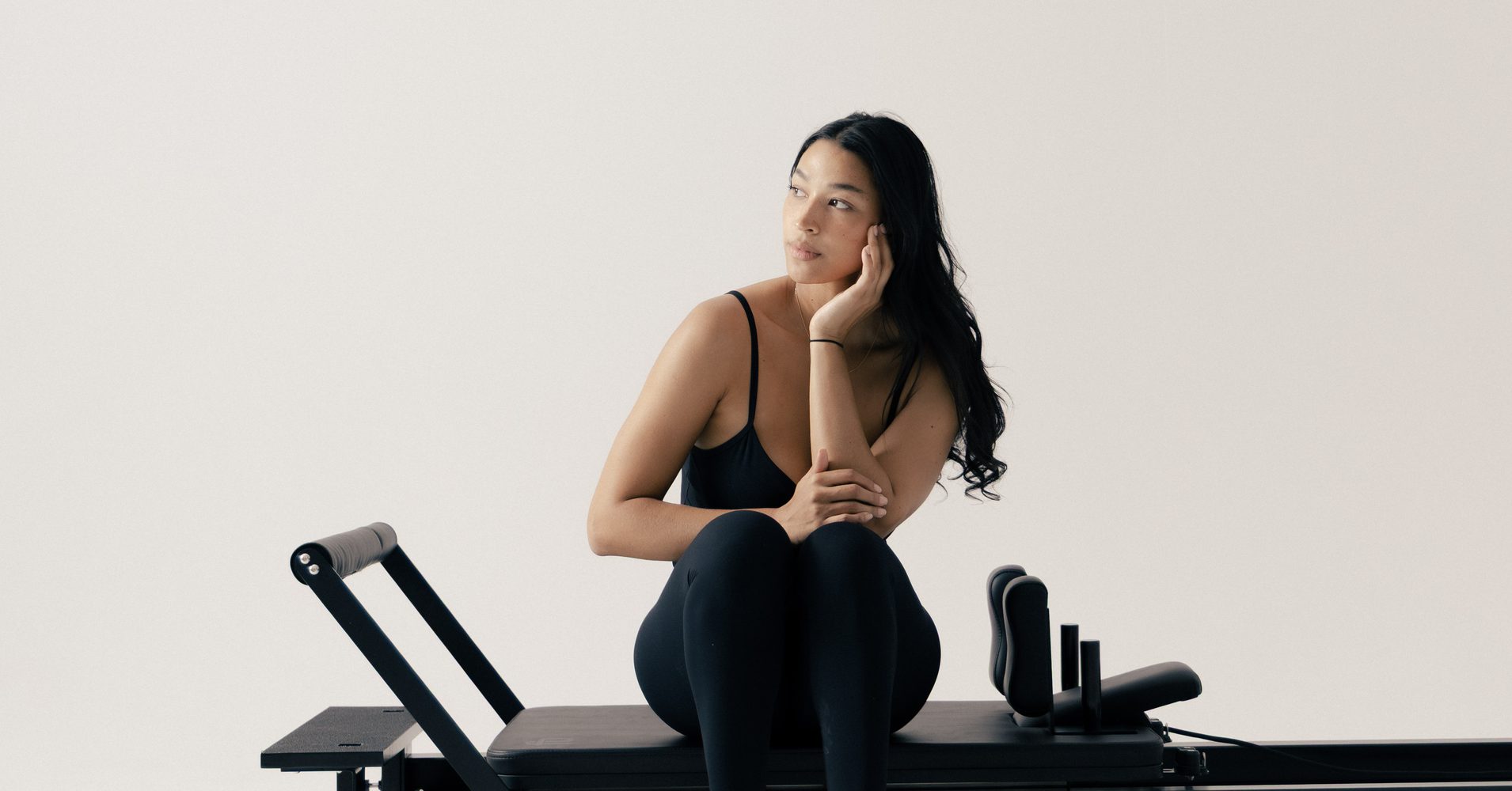 Woman seated on a FitBoutique Space Black reformer ready to begin a workout